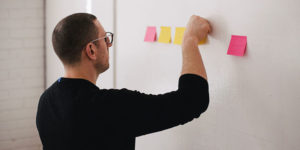 man pinning pink and yellow sticky notes on a white wall