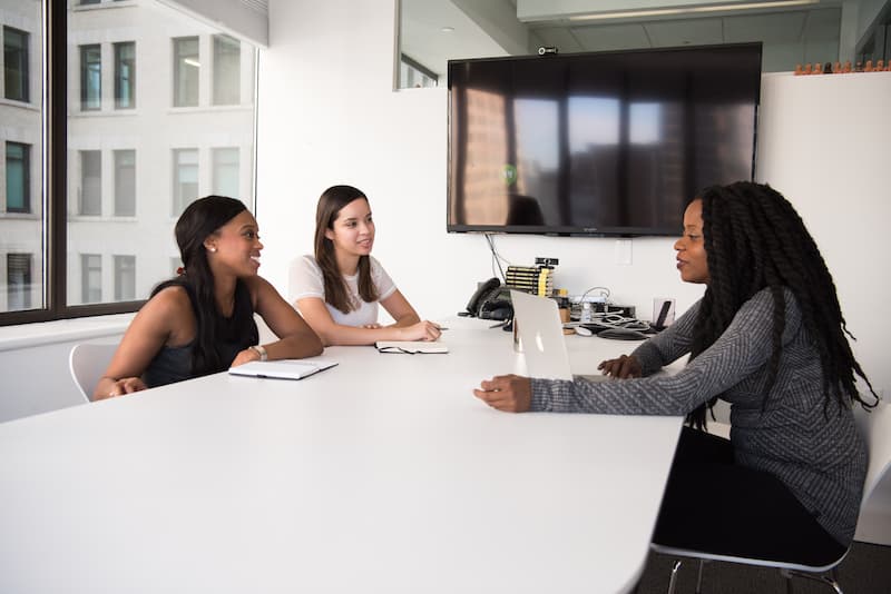 3 Frauen sitzen an einem weißen Schreibtisch und interviewen Feature Image For: Hiring Hacks, die Ihr Start-up jetzt nutzen sollte
