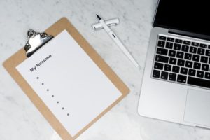 Top down photograph of a clipboard holding a piece of paper titled "My Resume" on the left and a laptop on the right.