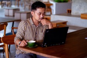 Angled profile photo of a man using his laptop at a cafe table. Feature Image for "How to Find Entry Level Jobs in Singapore"