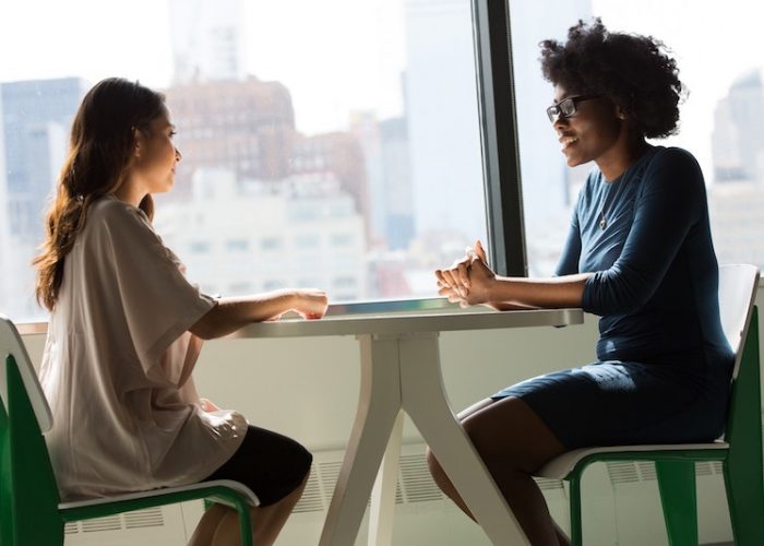 Two women sitting facing each other next to a window having a conversation. Feature image for the article, How to Answer the Most Common Interview Questions (with Examples)"