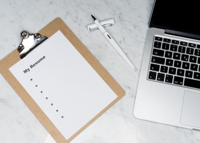 Top down photograph of a clipboard holding a piece of paper titled "My Resume" on the left and a laptop on the right.